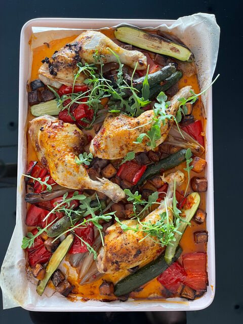A tray of roast chicken legs with red peppers, courgette and rocket leaves