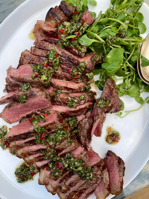 Sliced steak with a green herb and chilli sauce, next to a pile of salad leaves, on a white platter