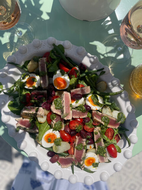 A salad of seared tuna slices, halved eggs, tomatoes, olives and green beans on a white plate